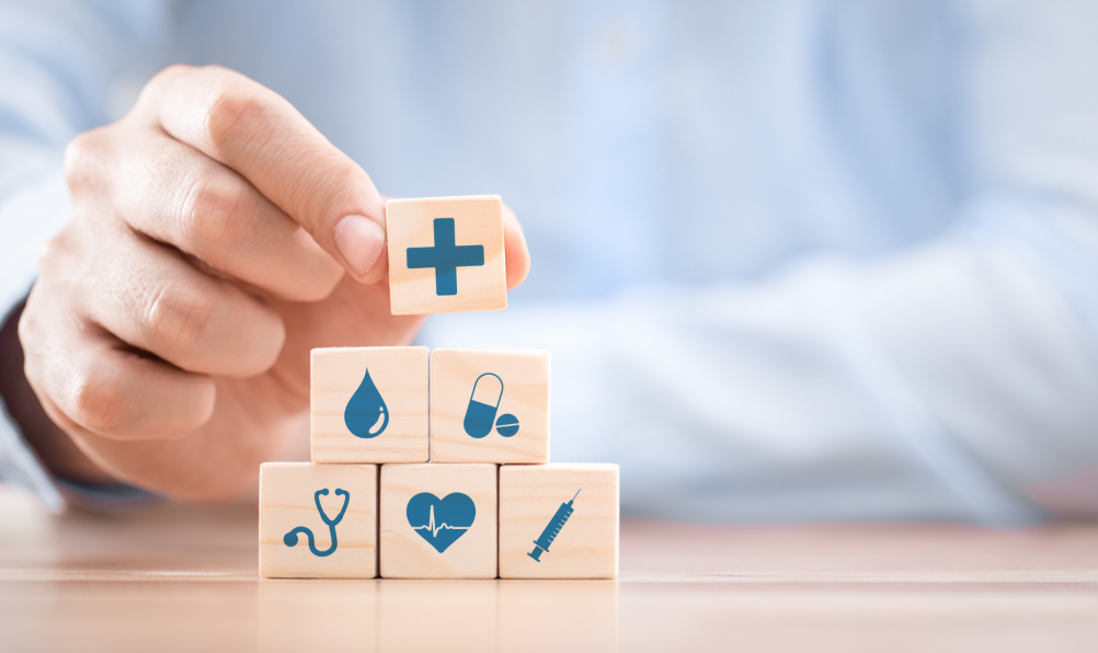Hand stacking wooden blocks with health and insurance icons.